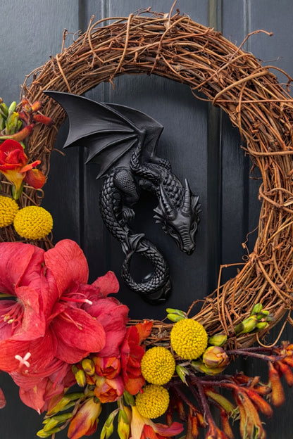 Decorative wreath with flowers and a dragon door knocker on a black front door 