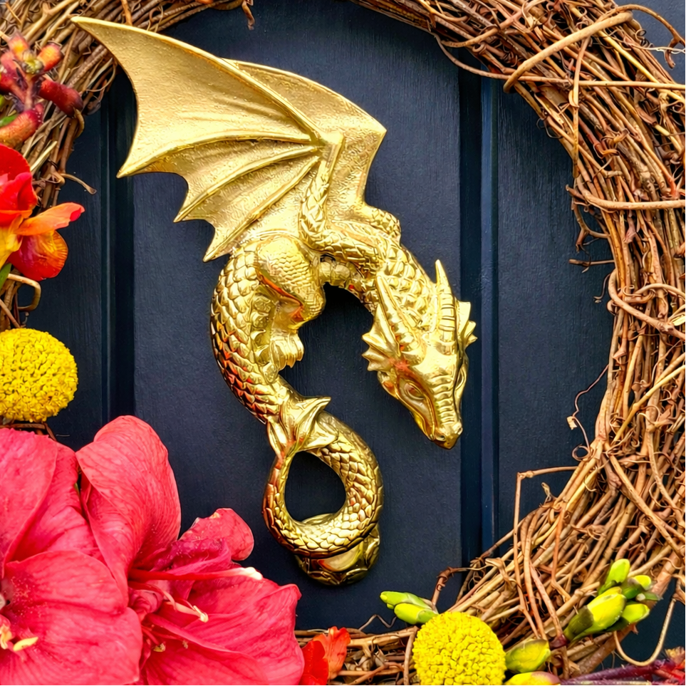 Decorative wreath with gold dragon door knocker, flowers, and natural elements on a dark background