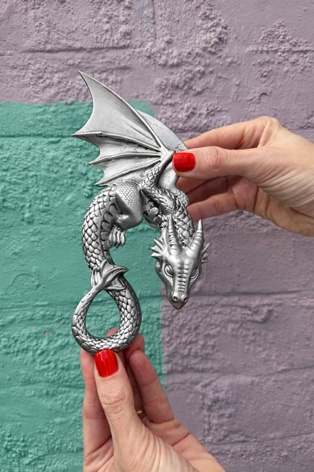 Silver dragon-shaped door knocker held by a hand against a textured wall.