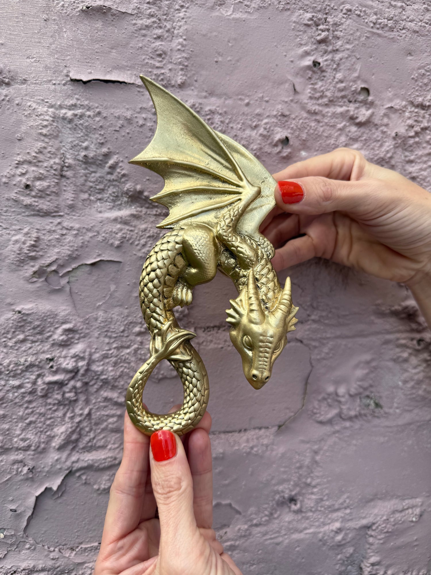 Gold dragon door knocker held by hands against a textured wall.
